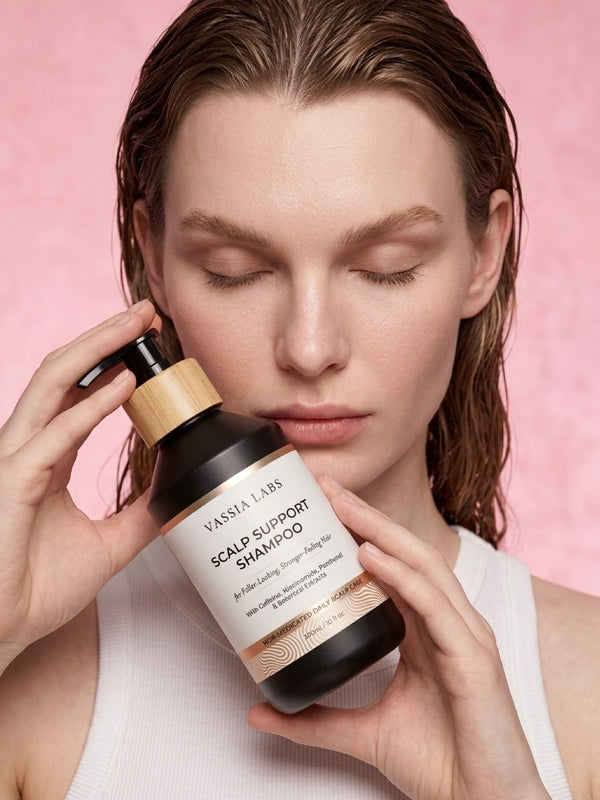 Model holding Vassia Labs shampoo beside her face against a pink background.